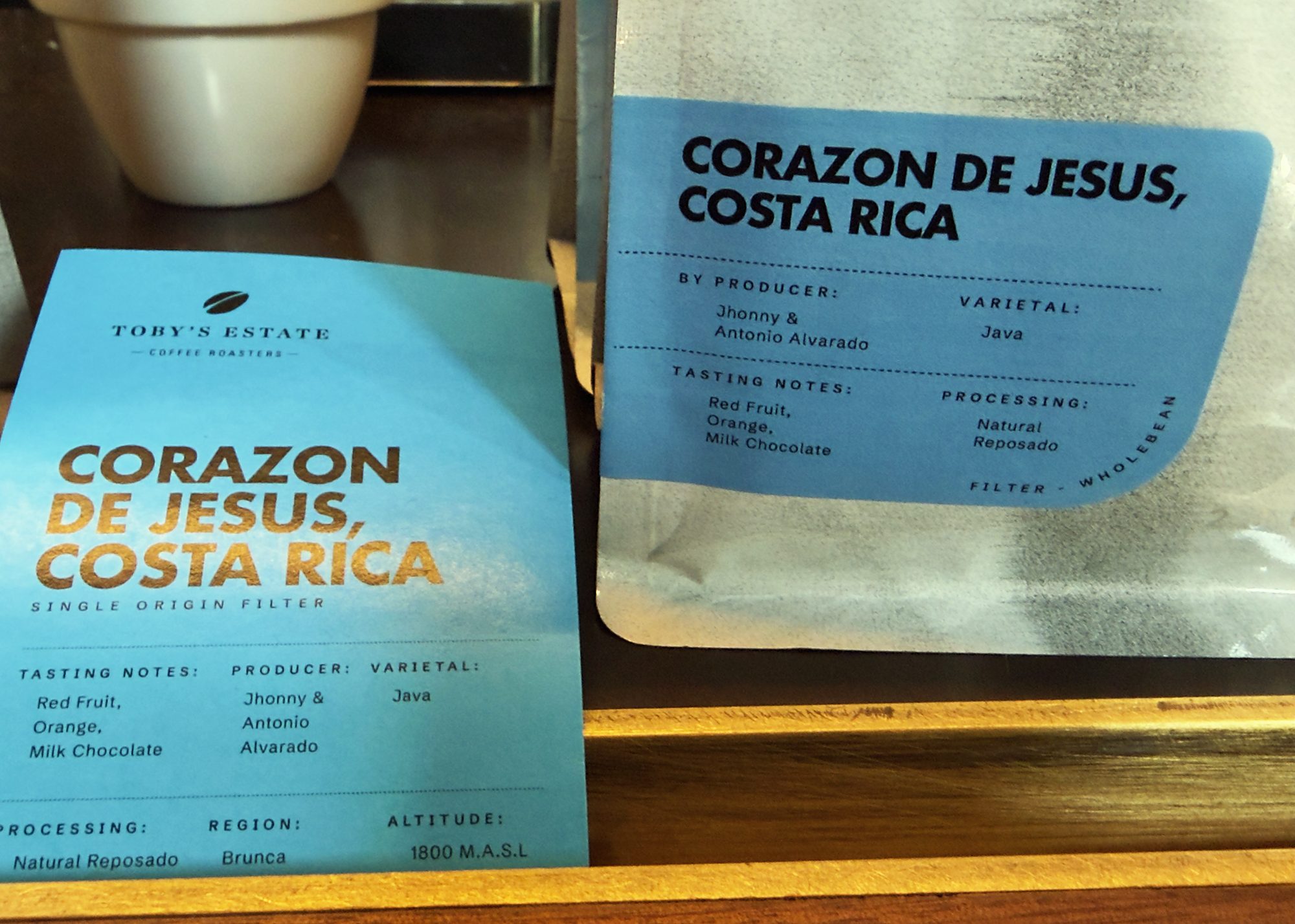 A shelf card and the bag it came from, side by side, both reading Corazon de Jesus, Costa Rica; the card adds region Brunca and altitude 1800 metres, which the bag does not print